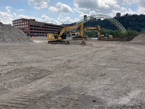 Excavators on site with the West End Bridge in view. Site work, August 2026