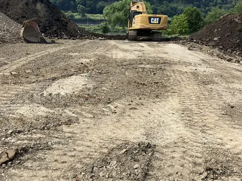 Tracked excavator on the graded site. Site work, August 2026