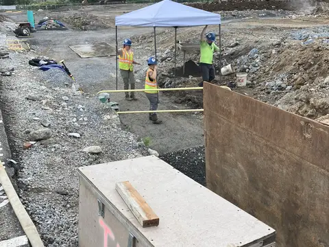 Crew working a utility trench under a canopy. Site work, August 2026