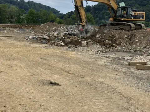 Excavator working the edge of the site. Site work, August 2026