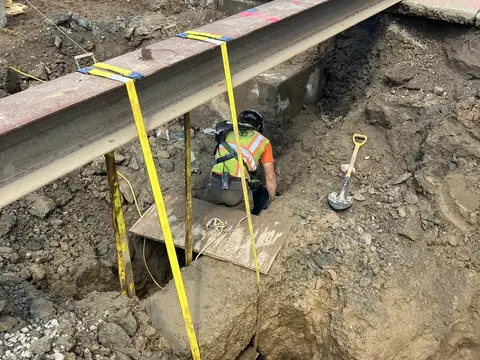 Utility work inside a shored excavation. Site work, August 2026